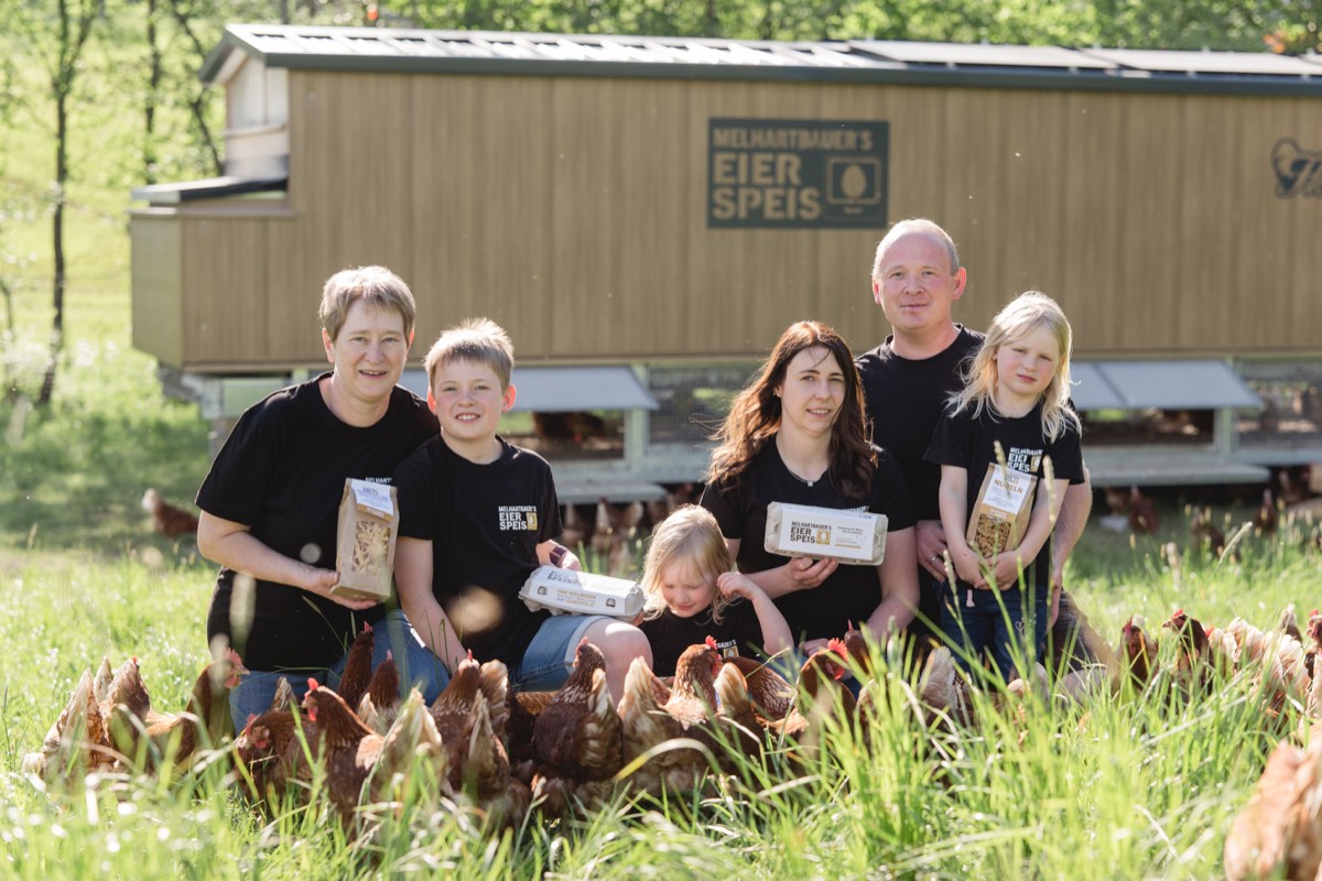 Drei Generationen der Familie Hollrieder mit Eiern und Nudeln vor dem mobilen Hühnerstall