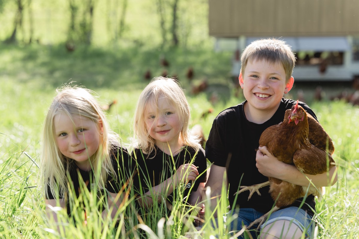 Die Kinder der Familie Hollrieder sitzen mit einer Henne im Gras vor dem Mobilstall